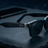 Óculos Ray-Ban Meta de terceira geração sobre superfície escura com reflexo ciano e celular desfocado ao fundo